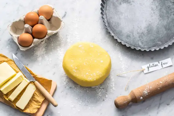 Impasto giallo brillante per pasta frolla senza glutine, pronto per essere steso. Ingredienti freschi e teglia per crostate a portata di mano.