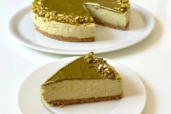Una fetta di goloso cheesecake al pistacchio, con la torta intera sullo sfondo.