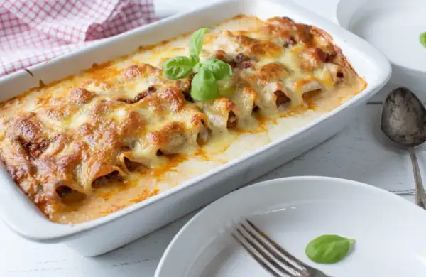 Cannelloni ripieni di carne macinata e mozzarella, cotti al forno e gratinati, guarniti con basilico fresco.
