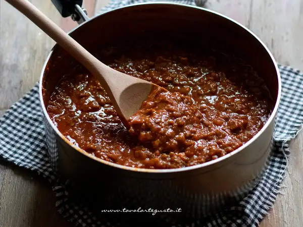 Un pentolone pieno di ragù alla bolognese, pronto per condire la pasta. Un cucchiaio di legno mescola la salsa ricca e saporita.