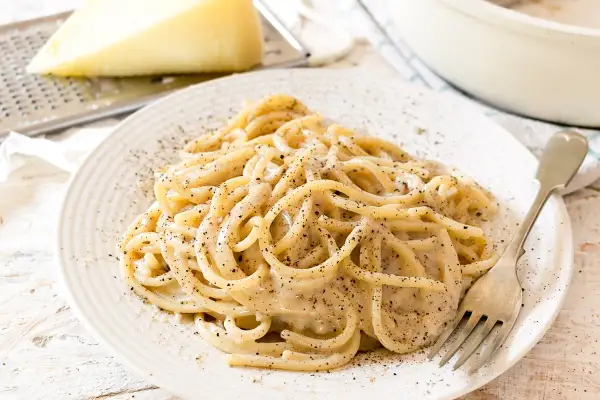 Un piatto di spaghetti fumanti, conditi con la cremosità del cacio e pepe, cosparsi di pepe nero macinato fresco.