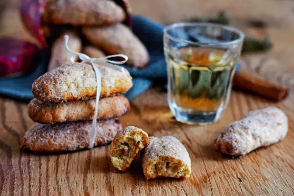 Ciambelline al vino dorate e zuccherate, una invitante pila legata da un nastro bianco, accanto a un bicchierino di vino e cannella.