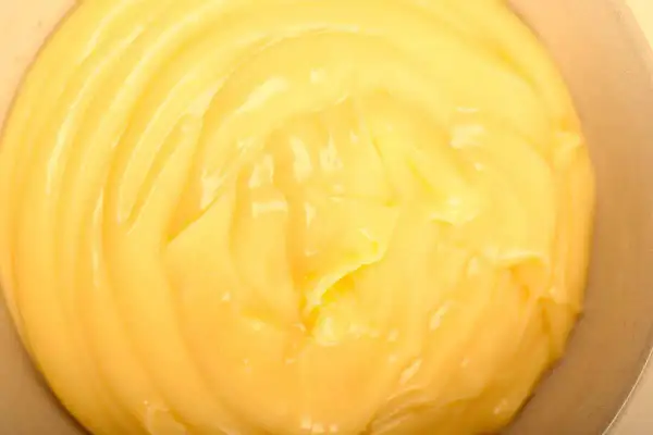 Close-up of smooth, creamy yellow pastry cream in a bowl, with visible swirls and highlights.