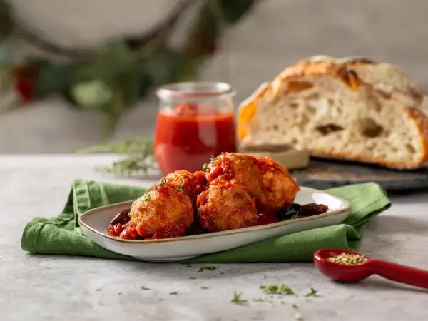 Polpette di cavolfiore dorate e saporite, immerse in un sugo rosso, servite con pane rustico e un rametto di erbe aromatiche.