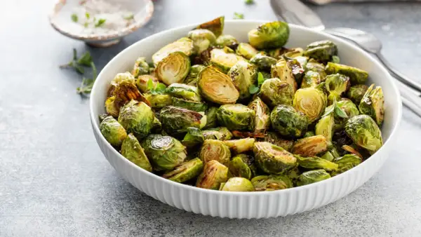 Ciotola piena di cavoletti di Bruxelles arrostiti, dorati e saporiti, guarniti con erbe fresche.