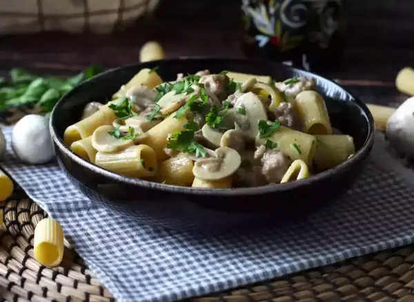 Piatto fumante di pasta funghi e salsiccia, guarnito con prezzemolo fresco. Un classico confortante.