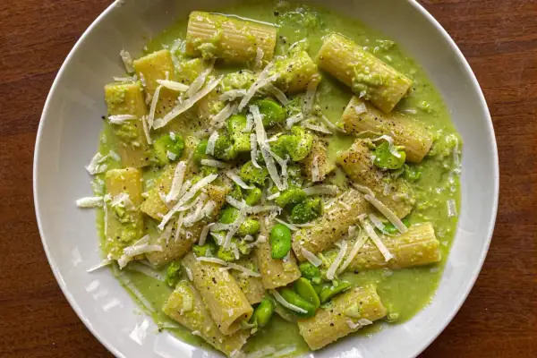 Rigatoni conditi con una cremosa salsa verde e fave fresche, guarniti con scaglie di parmigiano e pepe nero. Un piatto di pasta e fave che profuma di primavera.