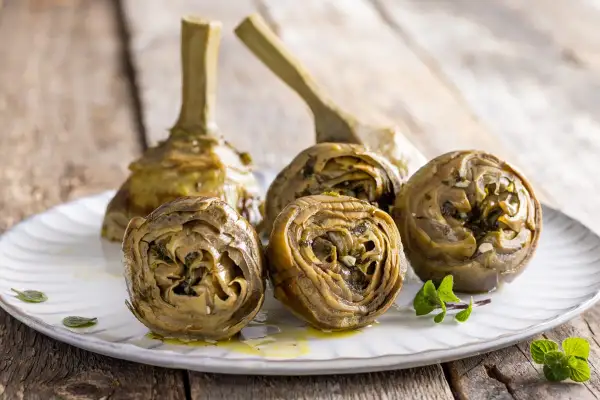 Carciofi alla romana ricetta: carciofi stufati con erbe aromatiche e aglio su un piatto bianco, pronti per essere gustati.