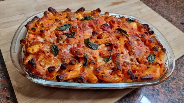 Un invitante piatto di pasta al forno napoletana, con pasta rigata dorata, sugo rosso e formaggio fuso, guarnito con foglie di basilico fresco.