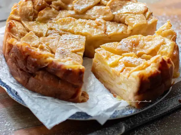 Una deliziosa torta di mele dorata, con fette di mela caramellate in superficie e una spolverata di zucchero a velo.