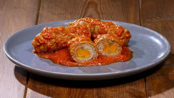 Involtini alla romana succulenti, avvolti in un sugo rosso intenso, con un cuore dorato visibile in sezione.