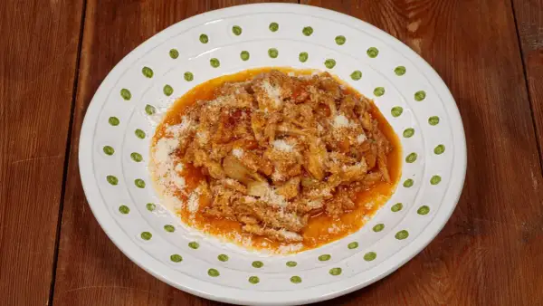 Un piatto di trippa alla fiorentina, saporita e ricca, cosparsa di parmigiano grattugiato, servita su un piatto bianco decorato.