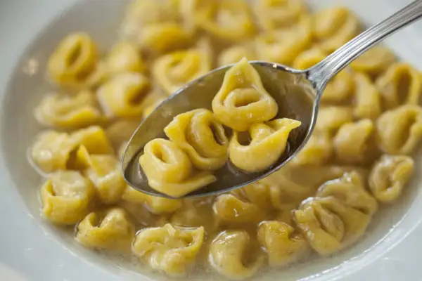 Un cucchiaio raccoglie deliziosi tortellini fatti in casa in brodo, pronti per essere gustati.