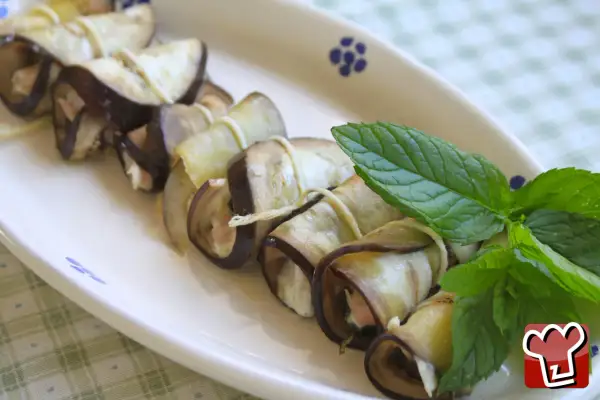 Deliziosi involtini di melanzane ripieni, guarniti con foglie di menta fresca su un piatto bianco.
